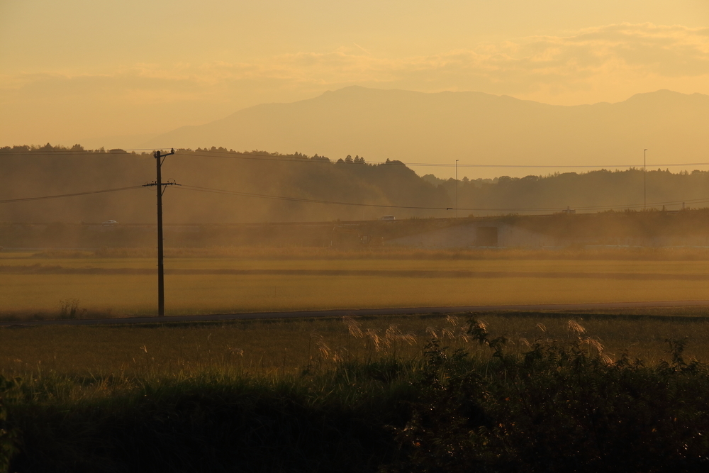 野焼きの煙が漂うの稲刈りを終えた田んぼと山や夕焼け空の写真
